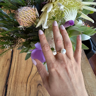 Hand with a ring and nude press-on nails in front of a bouquet of flowers on a wooden surface