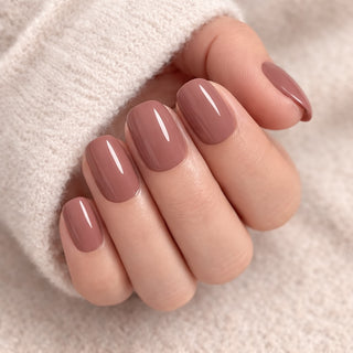Close-up of a hand with mocha brown colored press-on nails on a soft beige background