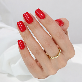 Hand with red press-on nails and a gold ring on a white background