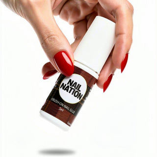 Hand holding a bottle of 'Nail Nation' nail glue with red nail polish on a white background