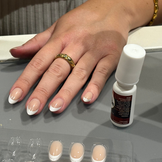 Hand with Nail Nation press-on nails and a bottle of nail glue on a grey surface