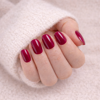 Close-up of a hand with cherry press-on nails on a soft pink background