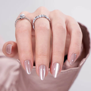 Close-up of a hand with glittery nail polish and rings on a neutral background