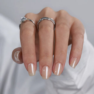 Close-up of a hand with beige nail polish and silver rings on a light gray background