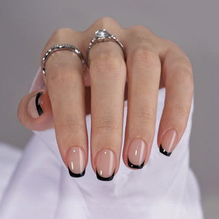Hand with beige nails and black tips wearing two silver rings on a neutral background