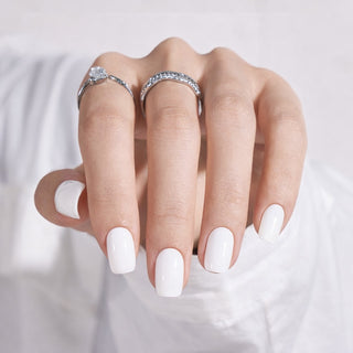 Hand with white press-on nails wearing two silver rings on a light background