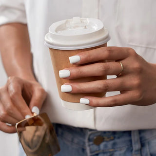 Person holding a paper coffee cup with a white lid, wearing a gold ring.