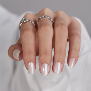 Close-up of a hand with beige nail polish and silver rings on a neutral background